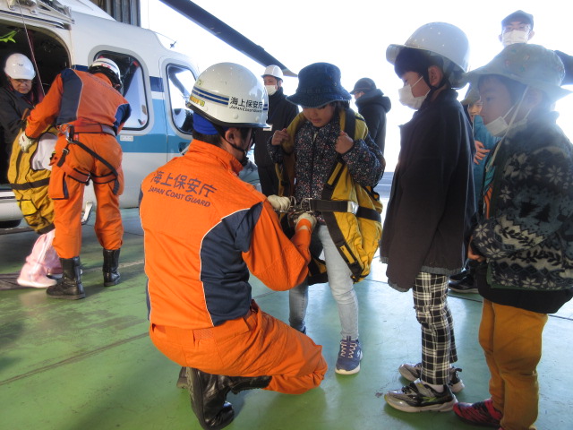 見学者に救難士がエバックハーネスを取り付けている状況